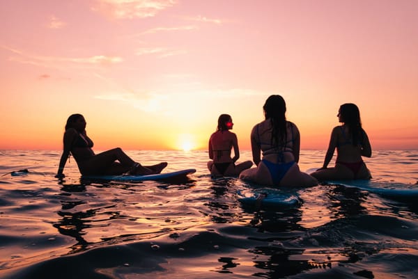 Four people sit on borards in the ocean, watching the sunset in Costa Rica.